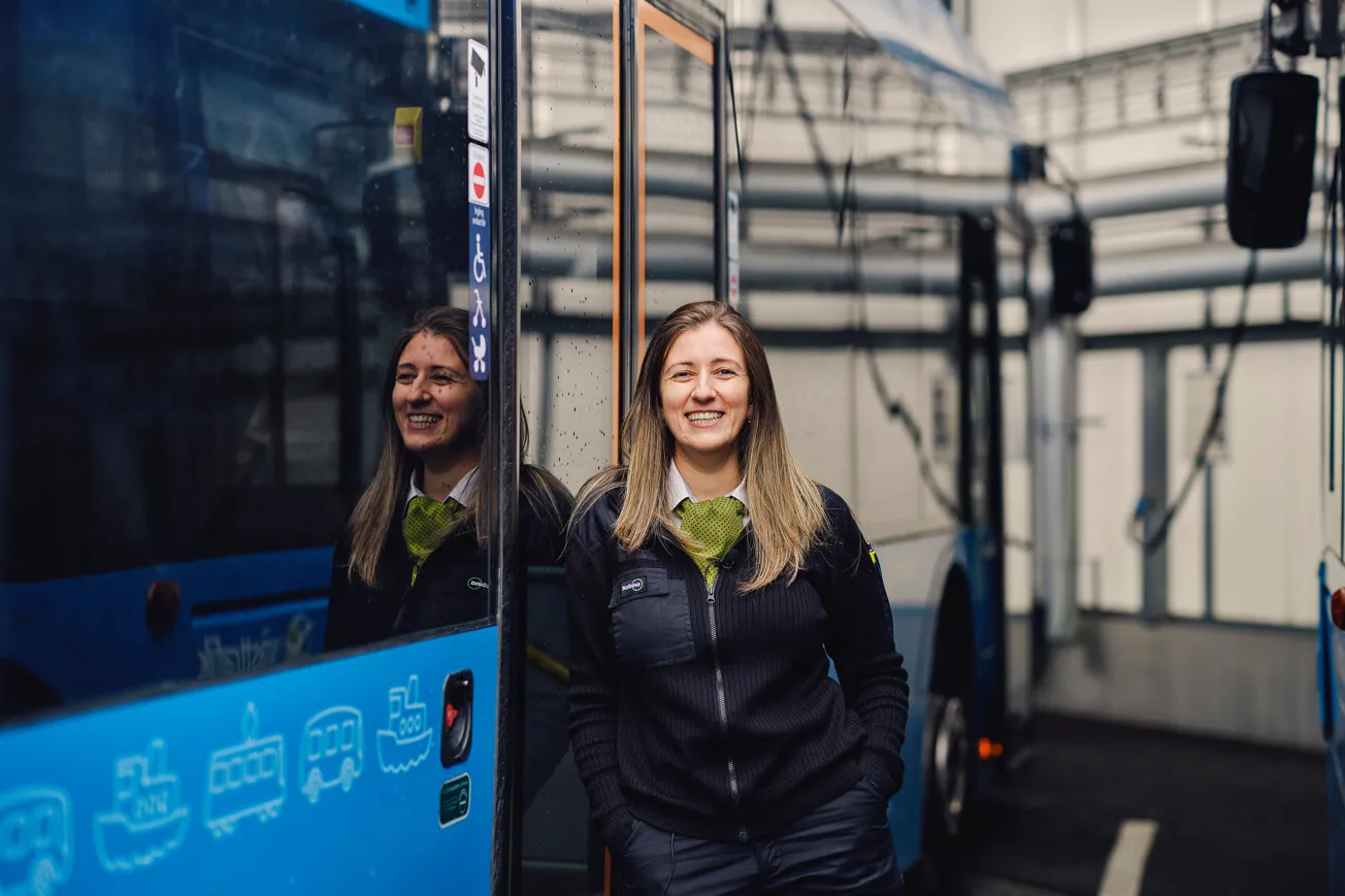 En kvinna som arbetar som bussförare står framför en blå buss.