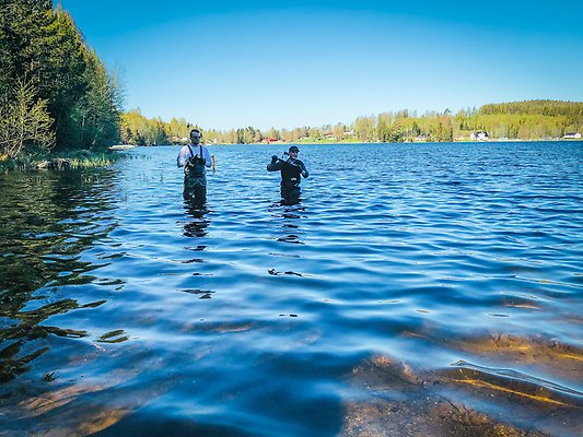 Två män står i en sjö och sätter ut en temperaturgivare för badtemperaturer.
